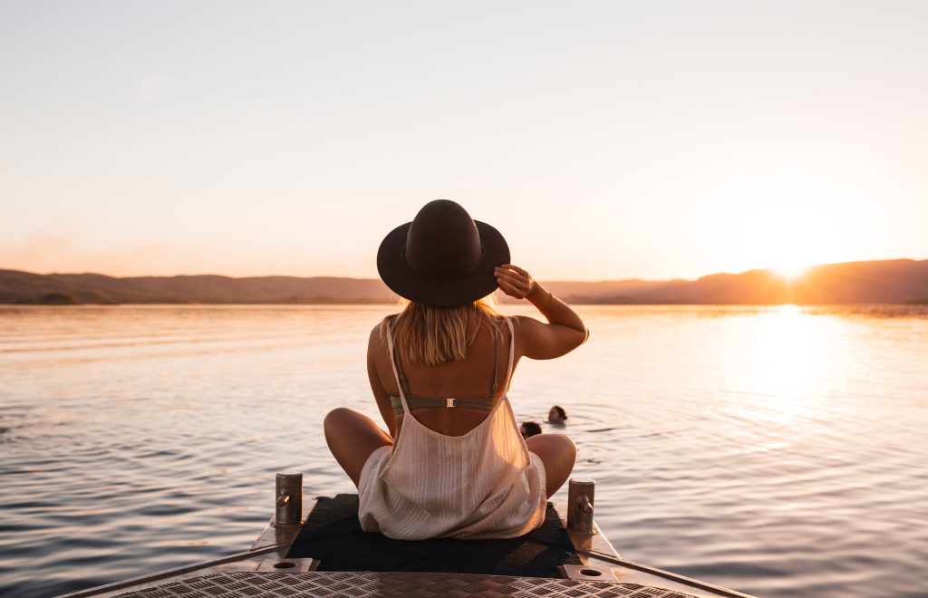 woman sitting lake pier surrounded by hills at sundown
